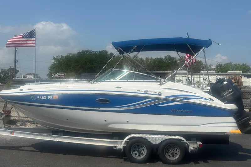 The Image of 2013 Hurricane SunDeck 2200 DC OB boat on trailer, blue and white design, American flag in background. - 0