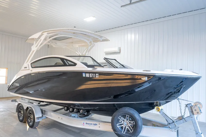 The Image of 2022 Yamaha Boats 275SD in a garage, sleek black design on a trailer. - 0