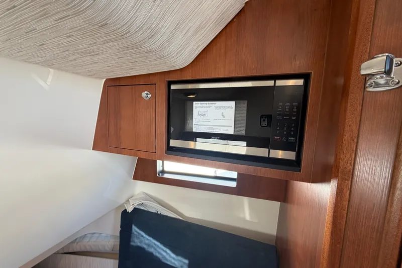 Slide: The Image of Interior of 2026 Pursuit S 358 Sport boat featuring a built-in microwave and wooden cabinetry. - 91