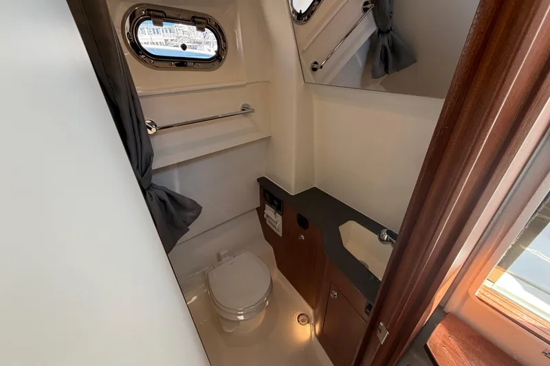 Slide: The Image of 2026 Pursuit S 358 Sport boat bathroom with toilet, sink, and porthole window. - 96