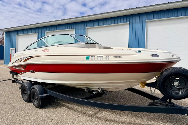 Slide: The Image of 2003 Sea Ray 200 Sundeck boat on trailer, parked near blue building. - 2