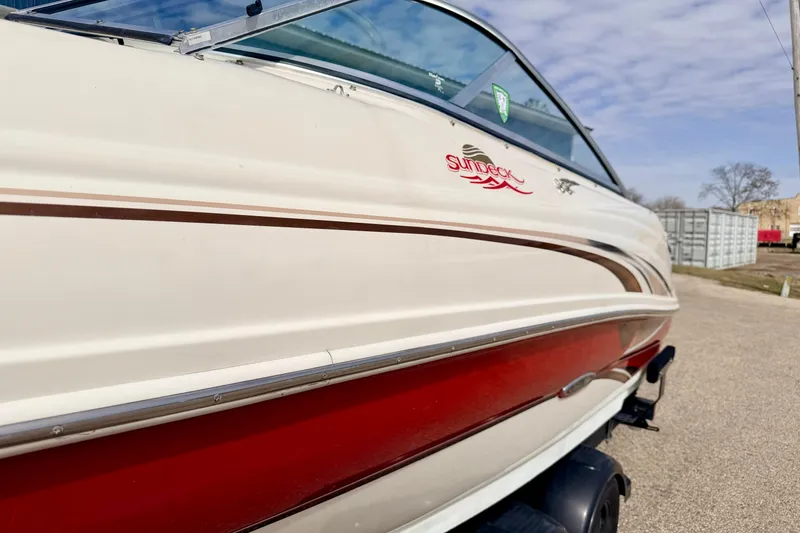 Slide: The Image of 2003 Sea Ray 200 Sundeck boat with red and white exterior, parked outdoors. - 63