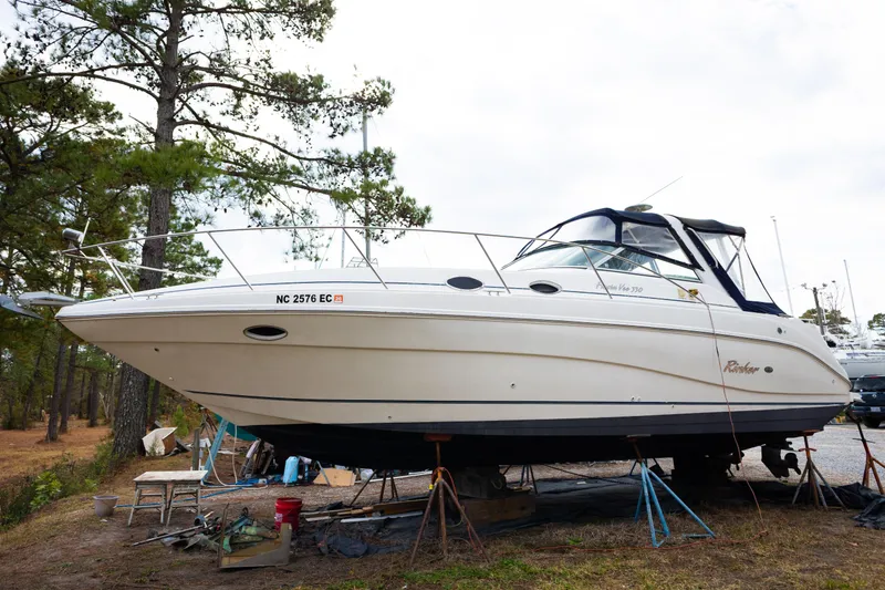 The Image of 2000 Rinker Fiesta Vee 330 boat on land, surrounded by trees and maintenance equipment. - 1