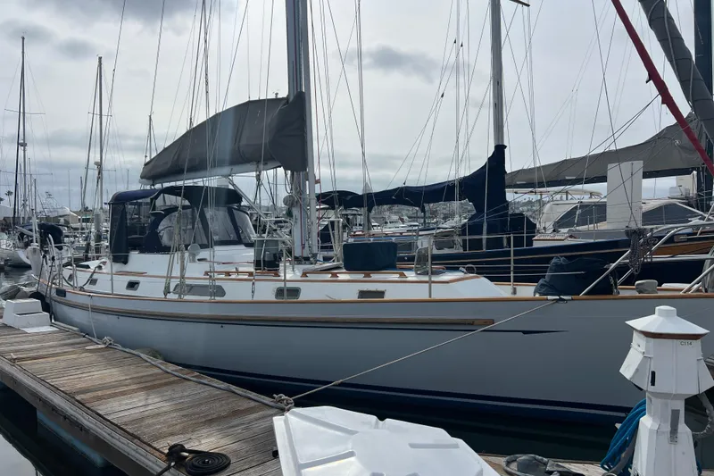 The Image of 1985 Passport 470 Center Cockpit sailboat docked at marina, overcast sky. - 0