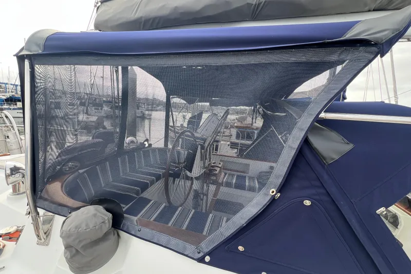 Slide: The Image of 1985 Passport 470 Center Cockpit sailboat with blue canvas cover and visible steering wheel. - 49