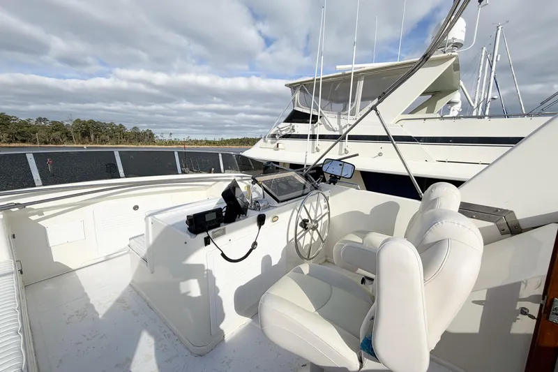 Slide: The Image of 1989 Jefferson Marquessa 52 yacht helm with white seating and steering wheel, docked under cloudy skies. - 42