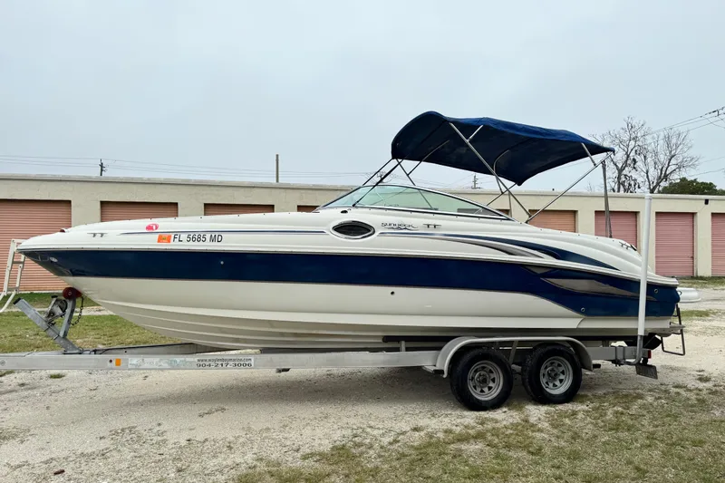 The Image of 2003 Sea Ray 240 Sundeck boat on trailer, blue and white, parked outdoors. - 1