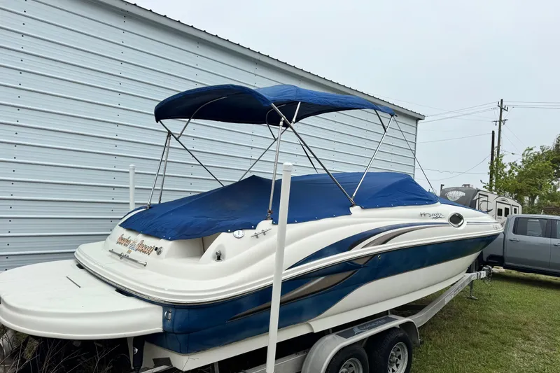 Slide: The Image of 2003 Sea Ray 240 Sundeck boat with blue cover on trailer, parked beside a metal building. - 31