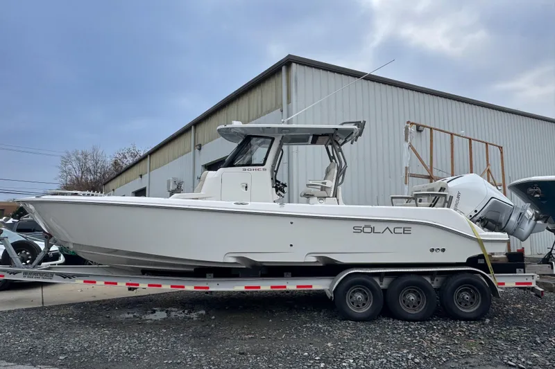 Slide: The Image of 2025 Solace 30 HCS boat on trailer, parked outside a warehouse. - 2