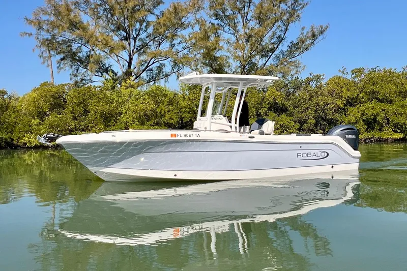 The Image of 2021 Robalo R242 Explorer boat on calm water with lush greenery background. - 0