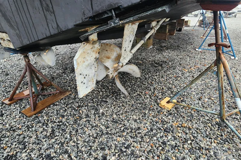 Slide: The Image of 1996 Bertram 46 Convertible boat hull and propeller on stands, gravel ground. - 27