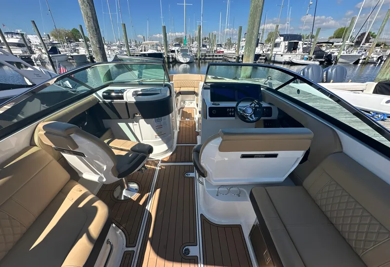 Slide: The Image of 2019 Sea Ray SLX 280 boat interior with tan seating and wood flooring at a marina. - 12