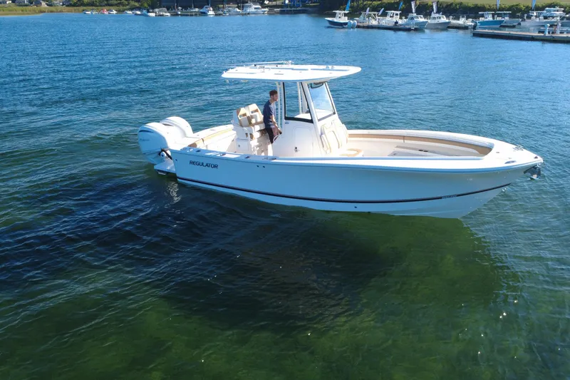 Slide: The Image of 2025 Regulator 25 boat cruising on clear blue water near a marina. - 13