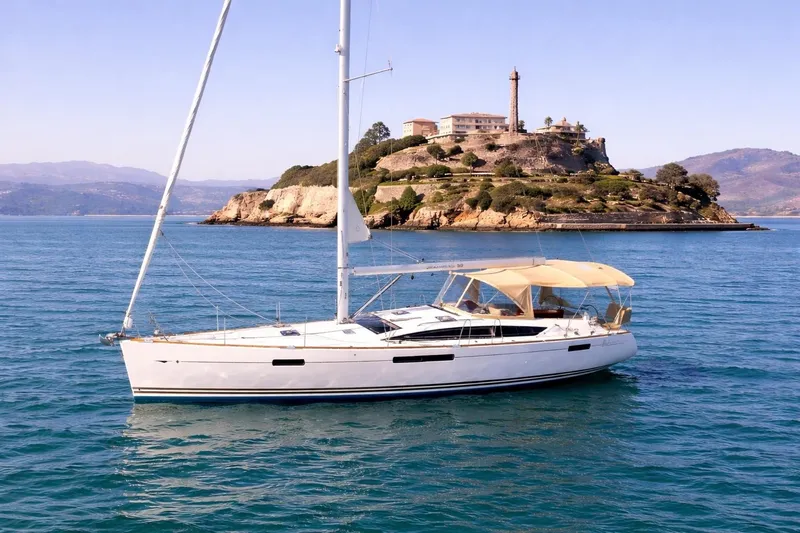 Slide: The Image of 2015 Jeanneau 53 sailboat on serene waters with scenic mountain backdrop. - 2