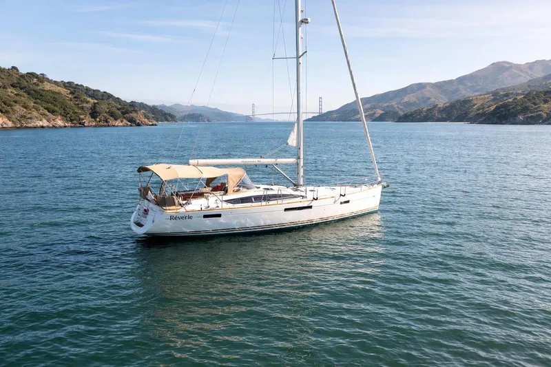 Slide: The Image of 2015 Jeanneau 53 sailboat "Rêverie" at sunset near a scenic coastal town. - 4