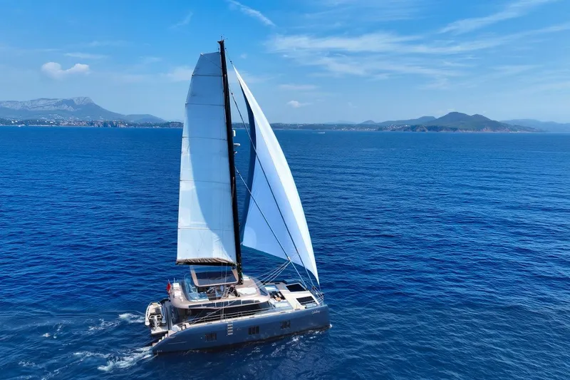 The Image of 2024 Sunreef 60 Sail Eco catamaran sailing on open blue sea with distant mountains. - 1