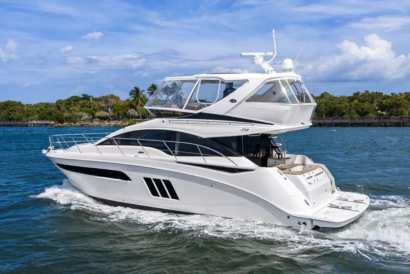 Slide: The Image of 2017 Sea Ray Fly 510 yacht cruising on blue water near lush shoreline. - 1