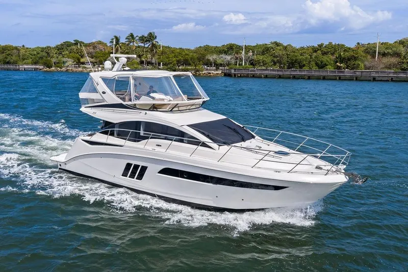 Slide: The Image of 2017 Sea Ray Fly 510 yacht cruising on blue water near a lush shoreline. - 14
