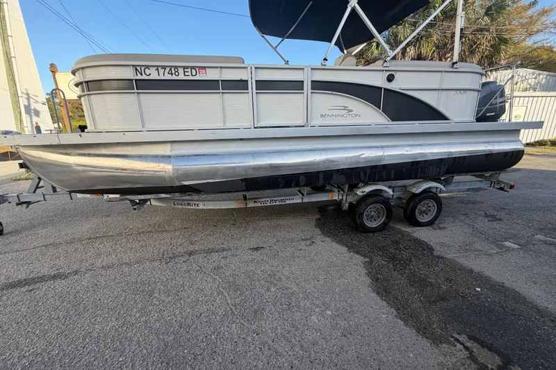 Slide: The Image of 2016 Bennington 22 SX pontoon boat on trailer, parked outdoors. - 22