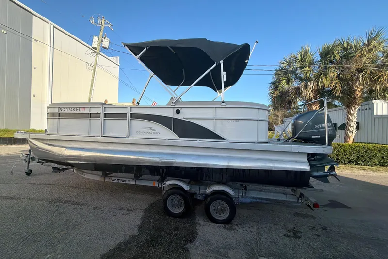Slide: The Image of 2016 Bennington 22 SX pontoon boat on trailer, with canopy, parked outdoors. - 28