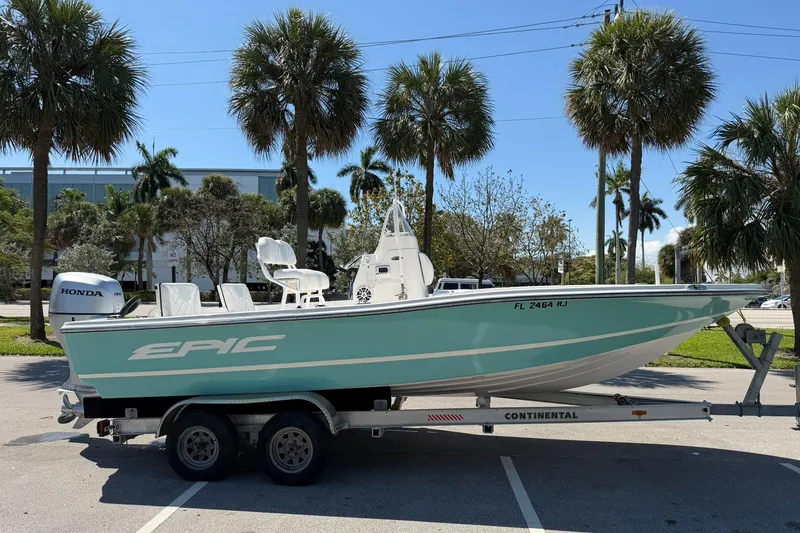 Slide: The Image of 2018 Epic 22SC boat on trailer, parked under palm trees, with Honda outboard motor. - 2