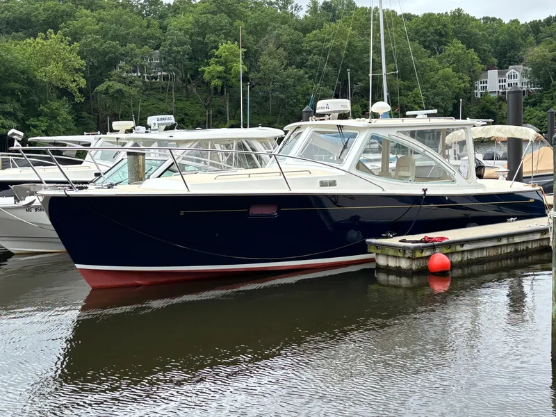 The Image of 2006 MJM 34z Express HT boat docked in a marina, surrounded by lush greenery. - 0