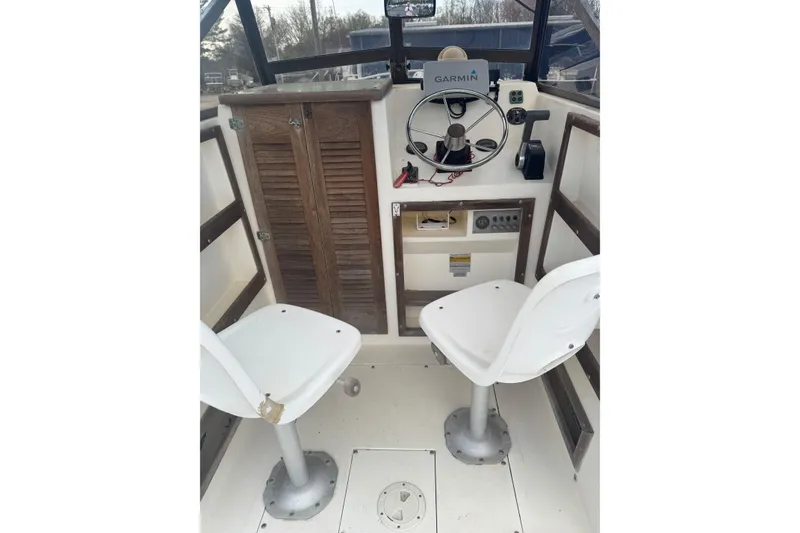 Slide: The Image of 1987 Mako 230 Walk Around boat interior with steering wheel and two white seats. - 4