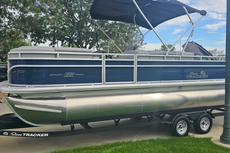 The Image of 2026 Sun Tracker SportFish 22 XP3 pontoon boat on trailer, parked outdoors. - 0