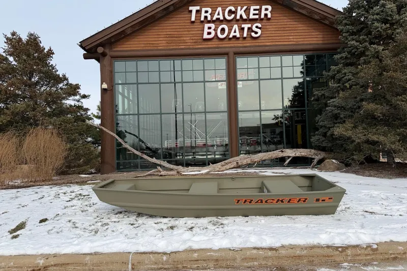 The Image of 2026 Tracker Grizzly 12 Jon boat displayed outside Tracker Boats store in snowy setting. - 0