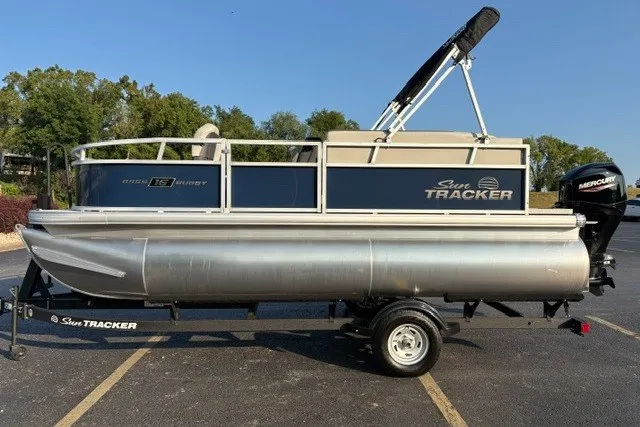 The Image of 2026 Sun Tracker Bass Buggy 16 XL Select pontoon boat on trailer, parked outdoors. - 0