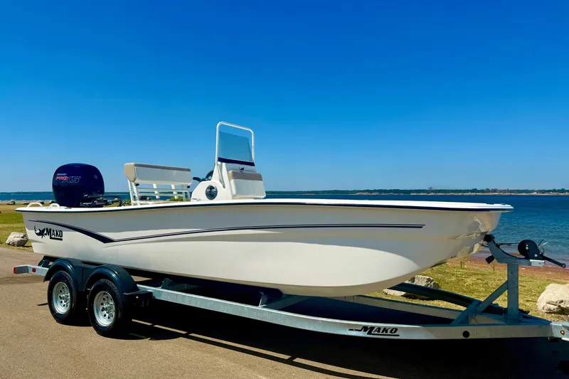 The Image of 2026 Mako Pro Skiff 19 CC boat on trailer by the water, under clear blue sky. - 0