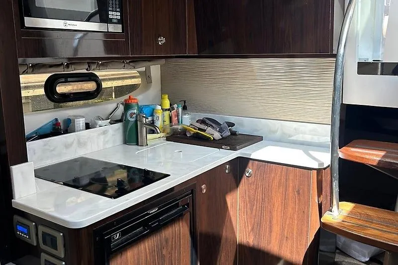 Slide: The Image of 2019 Sea Ray Sundancer 350 Coupe kitchen with stove, microwave, and wooden cabinetry. - 12