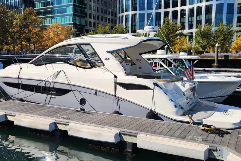 Slide: The Image of 2019 Sea Ray Sundancer 350 Coupe docked at a marina with modern buildings in the background. - 2