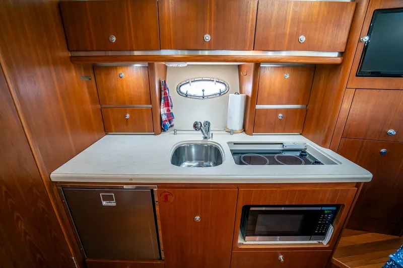 Slide: The Image of 2005 Tiara Yachts 3200 Open galley with wood cabinetry, sink, stove, and microwave. - 13