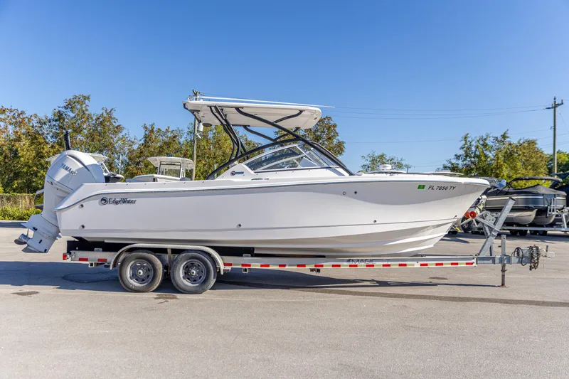 The Image of 2025 Edgewater 248CX Crossover boat on trailer, parked outdoors under clear blue sky. - 0