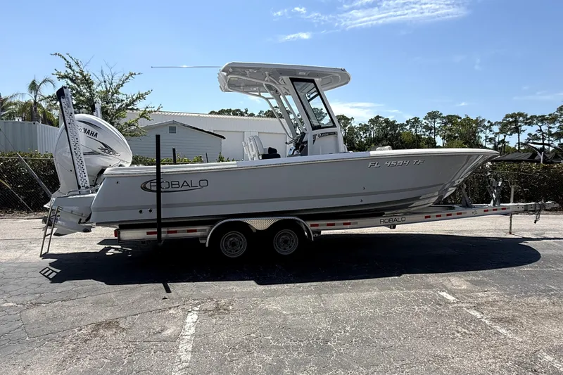 Slide: The Image of 2022 Robalo 266 Cayman boat on trailer, parked outdoors under clear sky. - 2