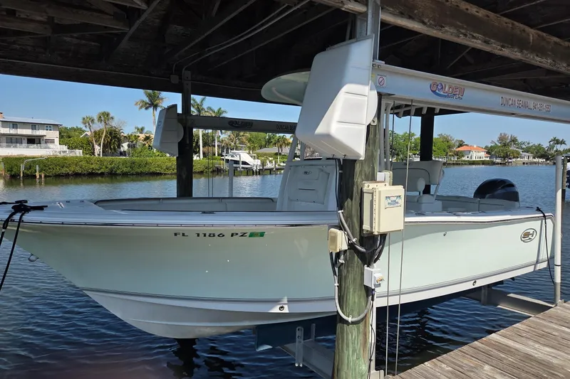 The Image of 2016 Sea Hunt Ultra 225 boat docked under a wooden shelter by the water. - 0