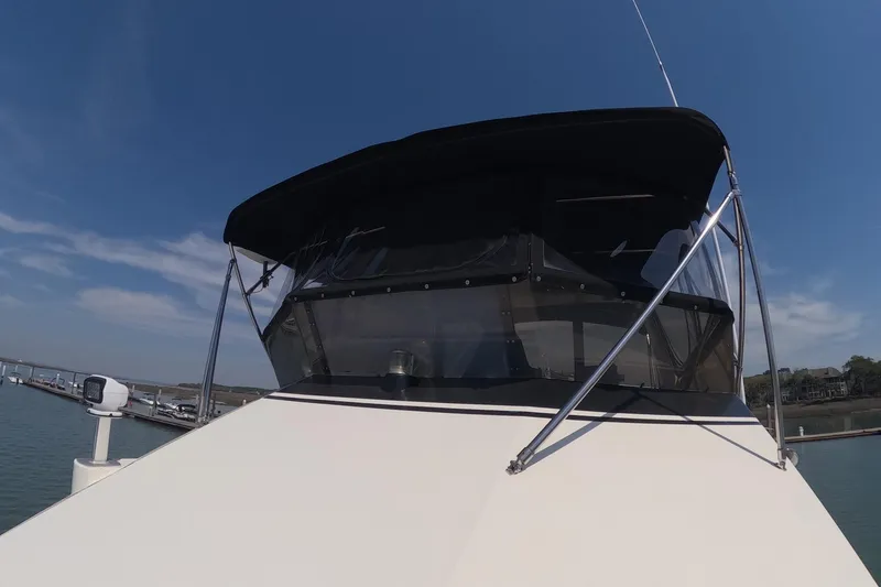 Slide: The Image of 1987 Hatteras 54 Motor Yacht with black canopy, docked under clear blue sky. - 54