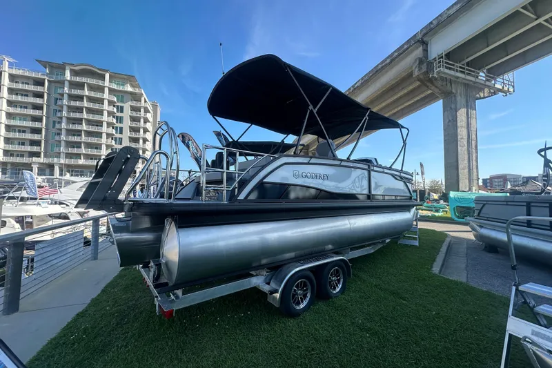Slide: The Image of 2026 Godfrey Monaco 235 SFL pontoon boat on trailer, displayed outdoors near marina. - 2