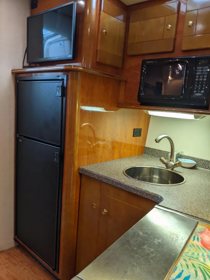 Slide: The Image of 2004 Rinker Fiesta Vee 410 yacht kitchen with wood cabinets, sink, fridge, and microwave. - 30