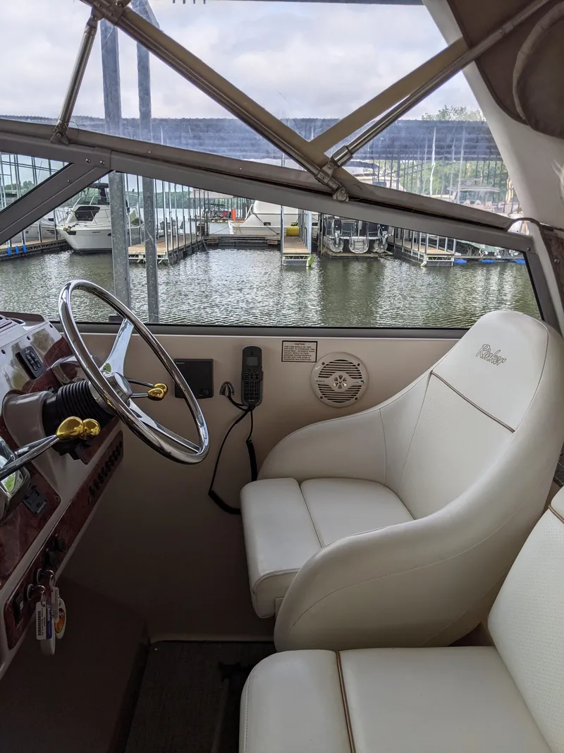 Slide: The Image of 2004 Rinker Fiesta Vee 410 helm with marina view, featuring white captain's chair and steering wheel. - 38