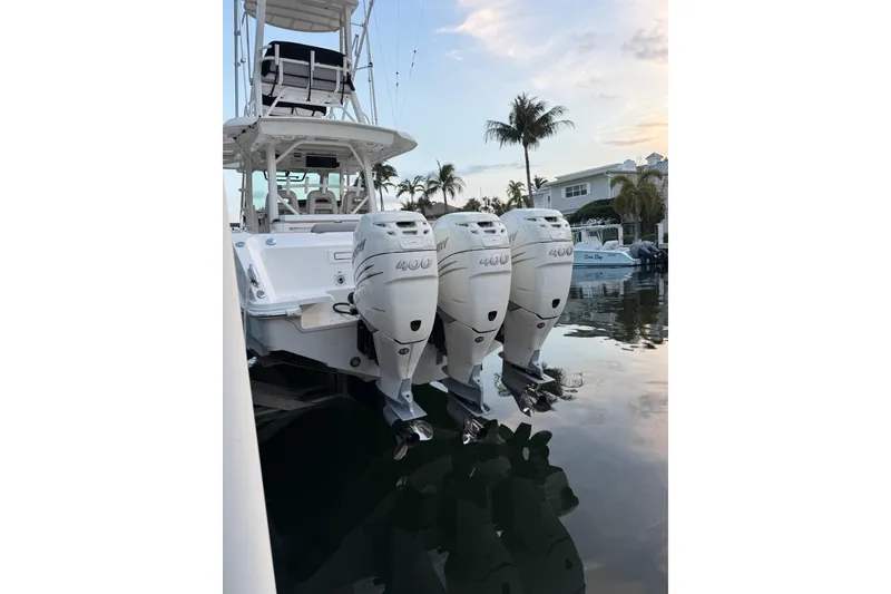 Slide: The Image of 2023 Boston Whaler 380 Outrage with triple 400 horsepower engines docked by palm trees. - 2