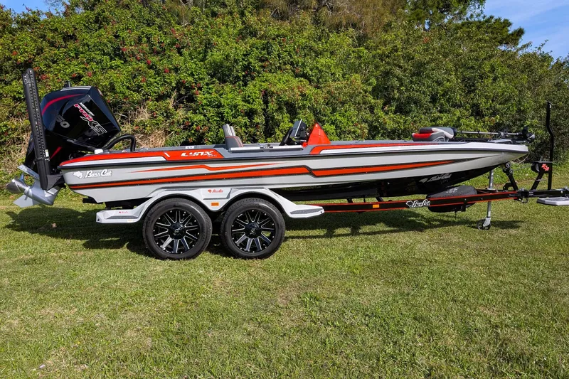 Slide: The Image of 2026 Bass Cat Lynx STS boat on trailer, parked on grass with lush greenery background. - 10