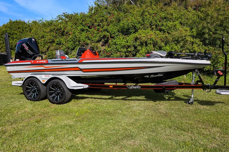 Slide: The Image of 2026 Bass Cat Lynx STS boat on trailer, parked on grass with lush greenery background. - 11