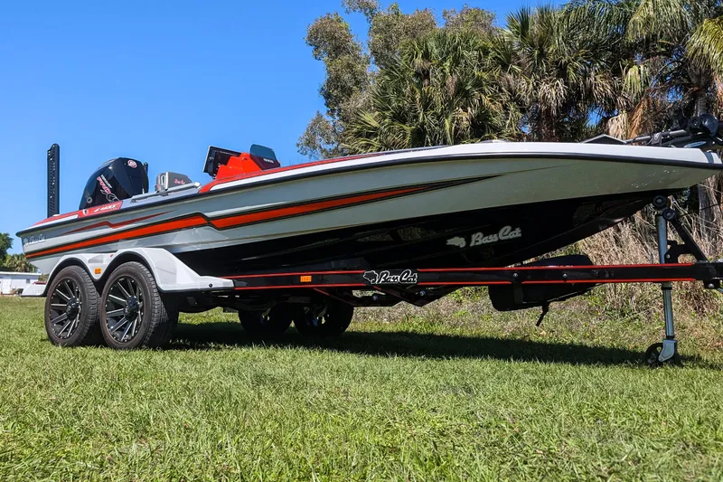 Slide: The Image of 2026 Bass Cat Lynx STS boat on trailer, parked on grass with trees in background. - 7