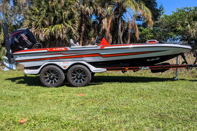 Slide: The Image of 2026 Bass Cat Lynx STS boat on trailer, parked on grass with palm trees in background. - 8