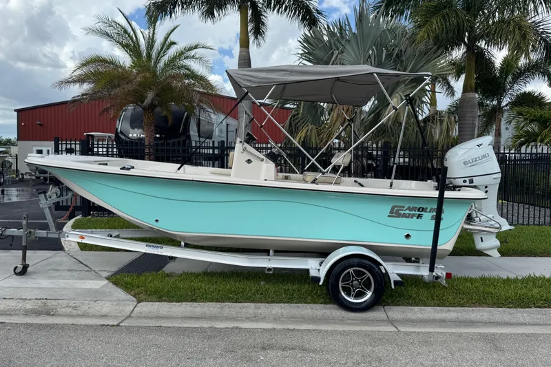 Slide: The Image of 2022 Carolina Skiff 19 LS boat on trailer, parked near palm trees. - 2