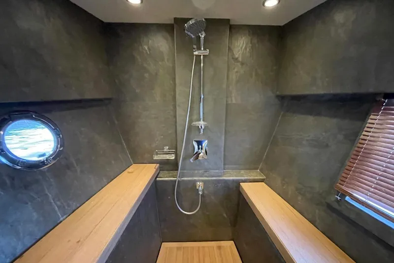 Slide: The Image of Luxurious shower area in 2018 Serenity 64 yacht with wooden benches and porthole window. - 61