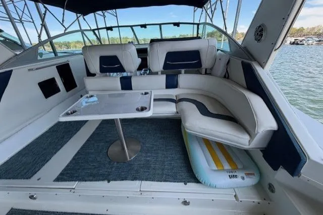 Slide: The Image of 1989 Sea Ray 460 Express Cruiser interior with cushioned seating and table, overlooking water. - 7