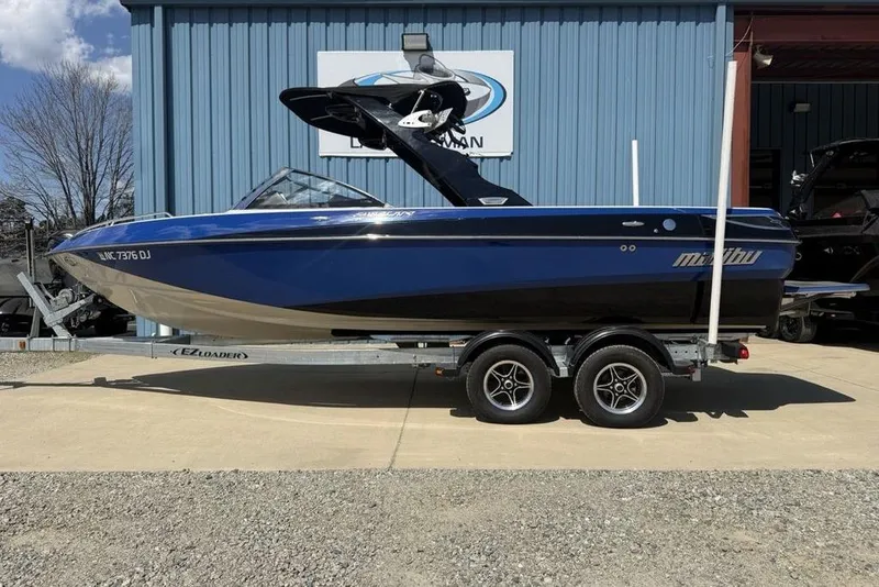 The Image of 2008 Malibu Sunscape 23 LSV boat on trailer, parked outside a blue building. - 1